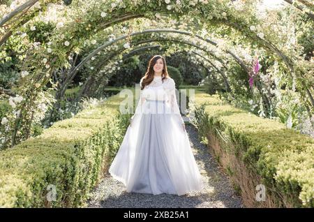 Fröhliche Frauen laufen im Garten unter Blumen in schieferblauem Kleid Stockfoto