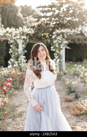 Glückliche Frauen, die ein fließendes blaues Schieferkleid in einem Rosengarten halten Stockfoto
