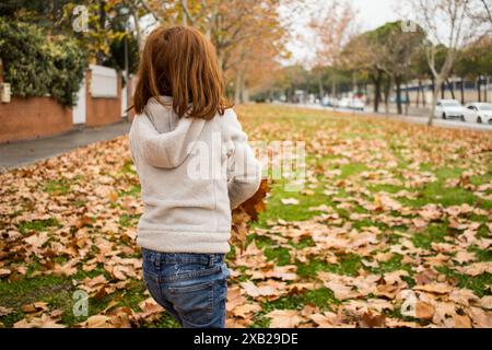 Mädchenhaar rot spielt mit Herbstlaub in einem Park mit Oberbekleidung. Außen. Jugendlich. Gesichtslos. Stockfoto