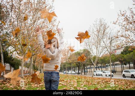 Mädchenhaar rot spielt mit Herbstlaub in einem Park mit Oberbekleidung. Außen. Jugendlich. Gesichtslos. Stockfoto