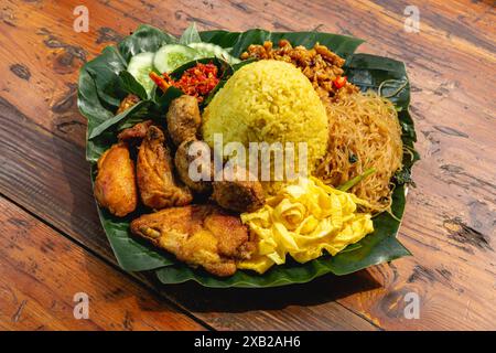 Nasi kuning oder Nasi Tumpeng, Dampfreis mit Kurkuma, gebratenem Huhn, Tempeh, Sambal und frischem Gemüse auf Bananenblättern Stockfoto