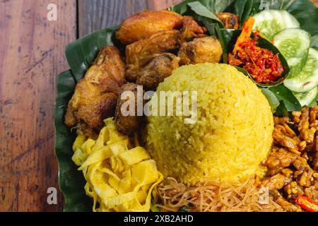 Nasi kuning oder Nasi Tumpeng, Dampfreis mit Kurkuma, gebratenem Huhn, Tempeh, Sambal und frischem Gemüse auf Bananenblättern Stockfoto