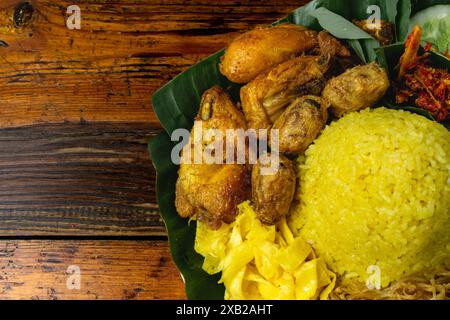 Nasi kuning oder Nasi Tumpeng, Dampfreis mit Kurkuma, gebratenem Huhn, Tempeh, Sambal und frischem Gemüse auf Bananenblättern Stockfoto
