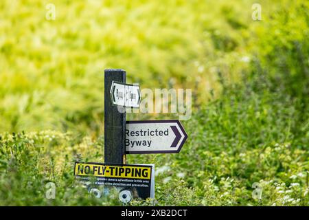 Wegweiser mit dem Richtungsweg, dem Restricted Byway und dem No Fly Tipping an einem Posten in der Landschaft von Wiltshire Stockfoto