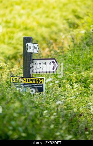 Wegweiser mit dem Richtungsweg, dem Restricted Byway und dem No Fly Tipping an einem Posten in der Landschaft von Wiltshire Stockfoto