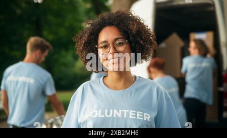 Porträt einer glücklichen hilfsbereiten Schwarzen Freiwilligen. Junge Erwachsene multiethnische Latina mit Afro-Haar, Brille, Lächeln, posieren für die Kamera. Konzept für humanitäre Hilfe und Freiwilligentätigkeit. Stockfoto