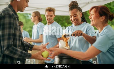 Das Konzept des Gebens: Obdachlose greifen auf kostenlose Freiwilligenmahlzeiten von einem multiethnischen Team von Freiwilligen zu. Humanitäre Hilfe Hilfsorganisationen versorgen bedürftige Menschen mit Mahlzeiten. Stockfoto