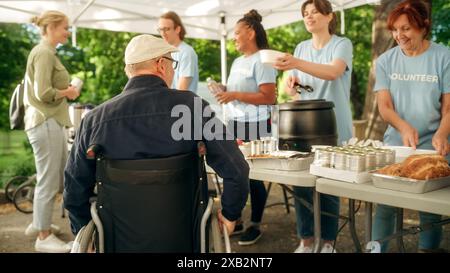 Positiver und lächelnder Mann mittleren Alters mit Behinderungen in einem Rollstuhl, der ein Wohltätigkeitsessen von einer Nahrungsmittelbank für humanitäre Hilfe erhält. Freiwillige helfen bedürftigen Menschen in der lokalen Gemeinschaft. Stockfoto