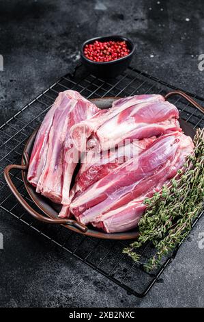 Rohe Lammschenkelschäfte in einer Stahlschale mit Kräutern. Schwarzer Hintergrund. Draufsicht. Stockfoto