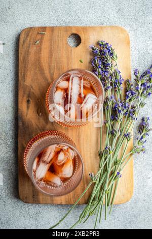 Zwei elegante Gläser Cognac-Cocktails, serviert auf einem rustikalen Holzschneidebrett, begleitet von frischen Lavendelzweigen, die eine raffinierte Mischung darstellen Stockfoto