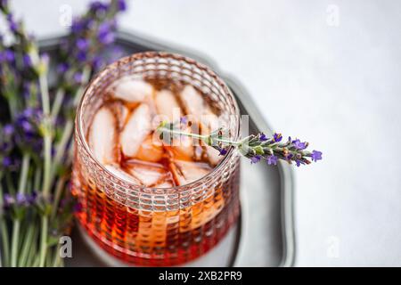 Ein raffinierter Cognac-Cocktail, serviert in einem strukturierten Glas mit Eiswürfeln, garniert mit einem frischen Lavendelzweig, auf einem Metalltablett mit einem Stockfoto