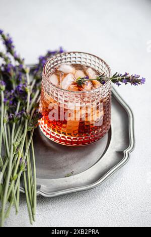 Eine elegante Präsentation eines Cognac-Cocktails, serviert in einem Kristallglas mit Eis, garniert mit einem frischen Lavendelzweig auf einer Vintage-Silbe Stockfoto