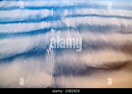 Eine Luftaufnahme des Zusammenspiels von Sand und Wasser erzeugt ein faszinierendes abstraktes Muster an einem Strand, das mit seiner Mischung aus Text einem Gemälde ähnelt Stockfoto