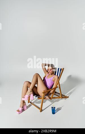 Trendige Frau mit blonden Haaren, die auf einem Liegestuhl in rosa Bikini sitzt. Stockfoto