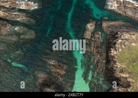Eine Aufnahme über dem Kopf, die den strukturellen Kontrast zwischen zerklüfteten fineart-Felsformen und dem ruhigen, smaragdgrünen Wasser einer Küstenregion feststellt. Stockfoto