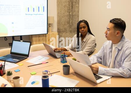 Verschiedene Teams arbeiten in einem modernen Coworking-Raum zusammen und analysieren Daten auf einem Projektorbildschirm Stockfoto