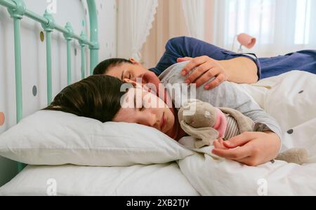 Zwei kleine Kinder, ein Junge und ein Mädchen, schlafen friedlich zusammen in einem hellen Schlafzimmer, während das Mädchen ein Kuscheltier umklammert Stockfoto