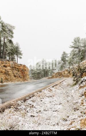 Eine ruhige Winterszene mit einer leicht verschneiten Straße, die sich durch die Sierra de Guadarrama in Spanien schlängelt, flankiert von verschneiten Bäumen und felsigen Hängen Stockfoto