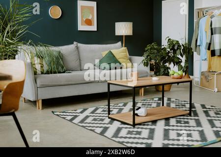 2-Sitzer-Sofa mit pastellfarbenen Kissen vor einem hölzernen Couchtisch mit geometrischem quadratischem schwarzen und weißen Teppich auf dem Boden Stockfoto