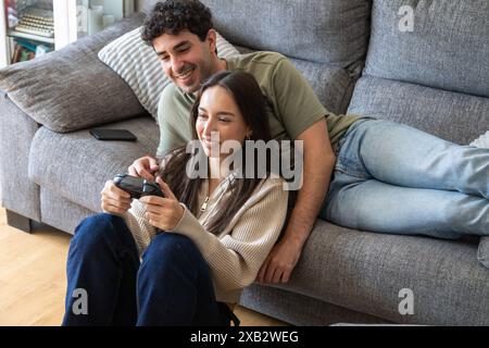 Ein junges Paar genießt einen lustigen Moment beim gemeinsamen Spielen von Videospielen auf einem grauen Sofa in seinem Wohnzimmer und zeigt Freude und Gesellschaft Stockfoto
