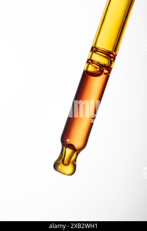 Hochauflösende Makroaufnahme einer kosmetischen Tropfpipette mit goldenem Hautpflegeserumtröpfchen auf weißem Hintergrund. Stockfoto