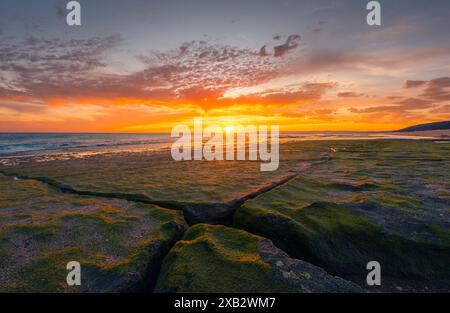 Moosbedeckte Felsen bei Sonnenuntergang am Atlanterra Beach mit lebendigem Himmel und Meer. Stockfoto