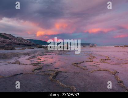 Der lebhafte Sonnenuntergang über dem ruhigen Atlanterra Beach in Cadiz mit strukturierten Felsformationen und reflektierenden Gezeitenpools. Stockfoto