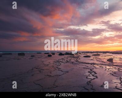 Der leuchtende Sonnenuntergang strahlt warme Farbtöne über dem felsigen Gelände von Atlanterra Beach aus, die sich in Gezeitenbecken spiegeln. Stockfoto