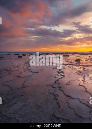 Der leuchtende Sonnenuntergang strahlt warme Farbtöne über dem felsigen Gelände von Atlanterra Beach aus, die sich in Gezeitenbecken spiegeln. Stockfoto