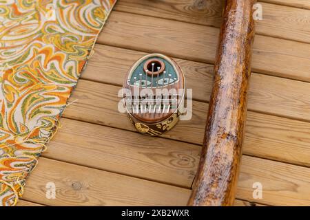 Ein Kalimba und Didgeridoo ruhen auf einem Holzboden auf einem farbenfrohen gemusterten Stoff, der das Wesen der Klangtherapie einfängt. Stockfoto