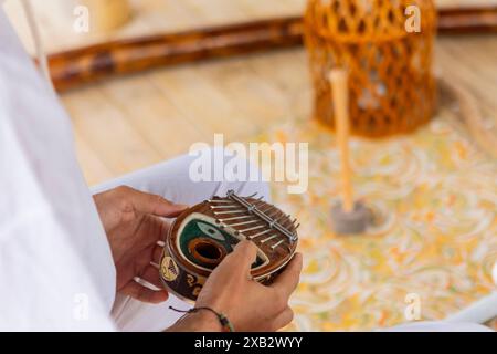 Hände einer anonymen Person, die während einer Klangtherapie ein Kalimba spielt, ein traditionelles afrikanisches Instrument, mit einem verschwommenen gong im B Stockfoto