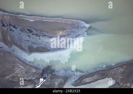 Ein Blick von oben, der die komplizierten Details eines teilweise gefrorenen Flusses erfasst, der sich durch die eisige Landschaft der isländischen Südküste schlängelt. Stockfoto