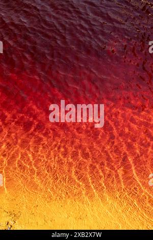 Leuchtende rote und orangene Muster auf der Wasseroberfläche, die in der Mine Riotinto in Huelva, Spanien, aufgenommen wurden und Umwelttexturen zeigen. Stockfoto