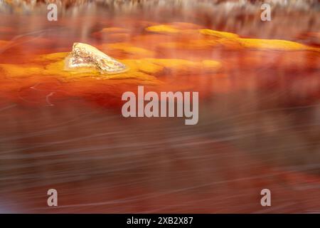 Eine abstrakte Aufnahme, die das leuchtende rote Wasser des Rio Tinto in Huelva, Spanien, mit einem Felsen, der einen Kontrast zwischen Textur schafft. Stockfoto