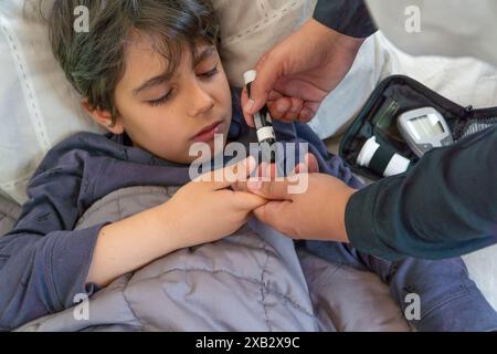 Die abgeschnittene, nicht erkennbare Mutter testet den Blutzuckerspiegel ihres Kindes, das auf einem Bett ruht, mit einem Glucometer. Stockfoto