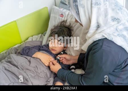 Unerkennbare Mutter testet den Blutzuckerspiegel ihres auf einem Bett ruhenden Kindes mit einem Glukometer Stockfoto