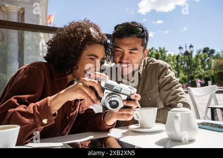 Ein multiethnisches Paar, bestehend aus einem Chinesen und einer hispanischen Frau, teilt einen freudigen Moment, während es Fotos auf einer Vintage-Kamera in einem Outdoor-C ansieht Stockfoto