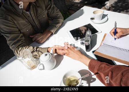 Ein multiethnisches Paar, ein Chinese und eine hispanische Frau, die Hände halten, während sie sich in einem Café in Madrid, Spanien, entspannen. Sie teilen sich einen Tisch mit Tassen Cof Stockfoto
