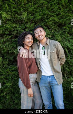 Ein multiethnisches Paar, bestehend aus einem Chinesen und einer hispanischen Frau, lächelt und posiert vor einer üppigen, grünen Kulisse in Madrid, Spanien. Sie strahlen h aus Stockfoto
