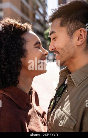 Ein fröhlicher chinesischer Mann und eine hispanische Frau teilen einen zärtlichen Moment, lächeln und betrachten einander liebevoll an einem sonnigen Tag in Madrid, Spanien. Das u Stockfoto