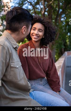 Ein multiethnisches Paar, ein Chinese und eine hispanische Frau, verbringen einen echten Moment im Freien in Madrid, Spanien. Die Frau lächelt den Mann an, Show Stockfoto