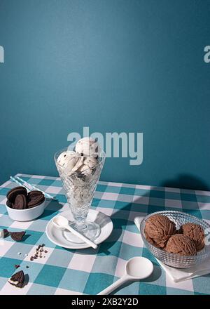 Eiskegel auf einem weißen Teller mit Sandwichkeksen auf einer blauen Tischdecke mit Schachbrettmuster, die an eine verspielte Dessertszene erinnern Stockfoto