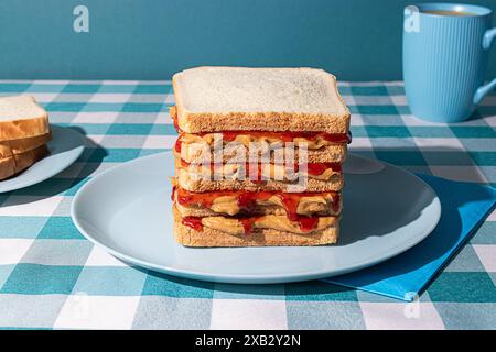 Erdnussbutter und Jelly Sandwich serviert auf einem blauen Teller, eine Tasse amerikanischen Kaffee und einige Brotscheiben auf blauem Hintergrund Stockfoto