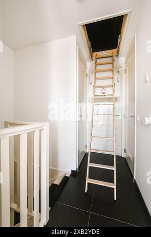 Ein moderner und sauberer Korridor mit einer klappbaren Holzleiterleiste, weißen Wänden und dunklem Boden in einem Amsterdamer Haus Stockfoto
