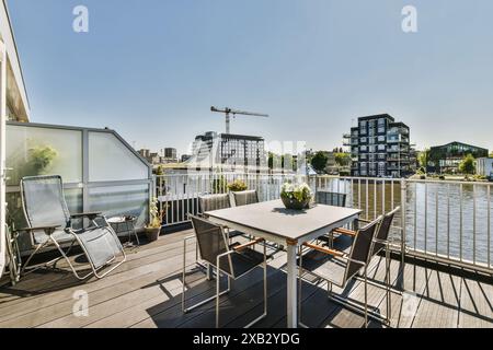 Genießen Sie die weitläufige Aussicht von einer sonnigen Dachterrasse in Oostzijde, Amsterdam, mit stilvollen Gartenmöbeln und modernen Gebäuden am Fluss Stockfoto