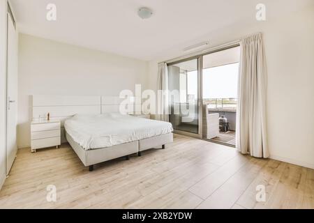 Helles und luftiges, modernes Schlafzimmer mit großem Bett, weißen Möbeln, fließenden Vorhängen und Zugang zu einem sonnigen Balkon in der Ottho Heldringstraat Stockfoto