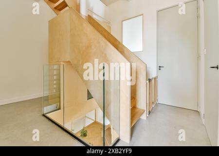 Zeitgenössisches Innenleben mit einer Holztreppe mit Glasbalustrade vor einem minimalistischen weißen Hintergrund mit einem Hauch von Grün. Stockfoto