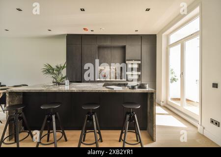 Elegante, moderne Küche mit eleganter Marmorarbeitsfläche, dunklen Holzschränken und Designer-Hockern unter der Frühstücksbar. Stockfoto