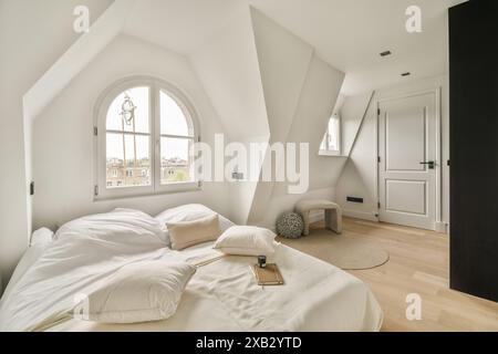 Ein luftiges, minimalistisches Schlafzimmer im Dachgeschoss mit geometrischen Winkeln, einem großen Bogenfenster und einer eleganten Einrichtung schafft einen ruhigen und modernen Raum. Stockfoto