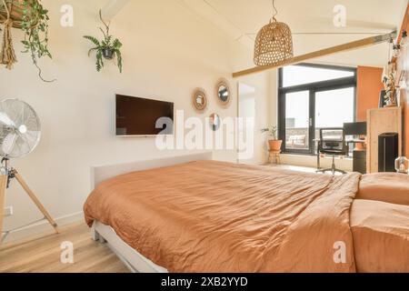 Ein gut beleuchtetes, modernes Schlafzimmer mit großem Fenster, Erdtönen und minimalistischen Möbeln. Das Zimmer ist mit modernen Designelementen wie ra ausgestattet Stockfoto